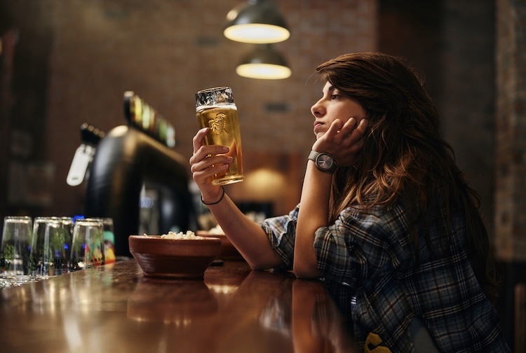 woman sitting alone at a bar counter looking at a beer