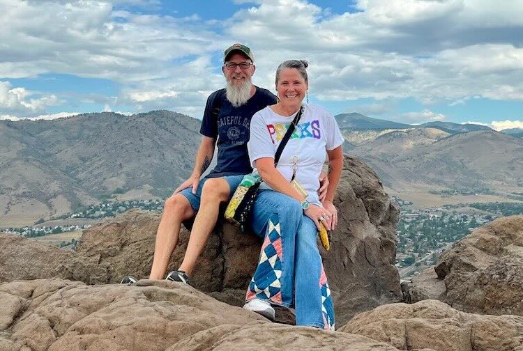 Rick and Tracey sit on a rock on top of a mountain