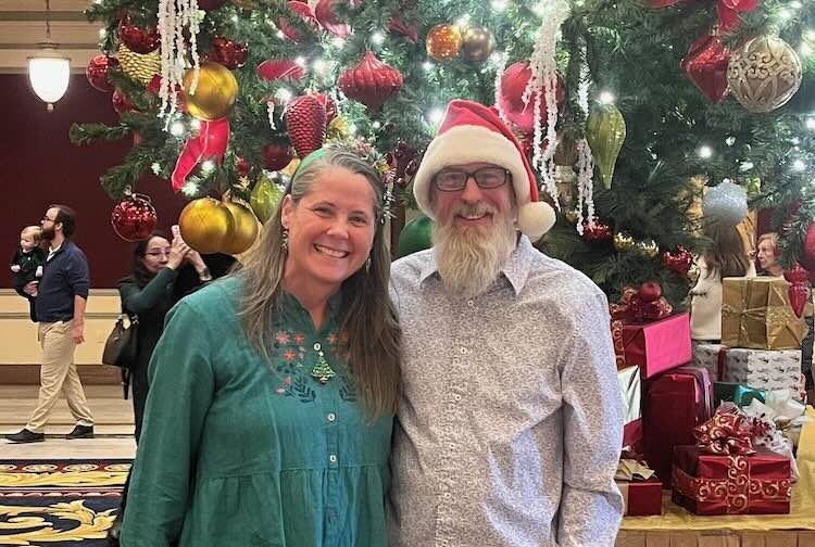 Tracey and Rick smile in festive clothing in front of the Christmas tree at The Jefferson Hotel in Richmond.