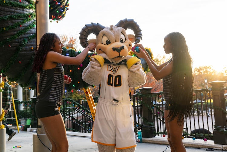 Rodney the Ram posed with two students who are adorning him with ornaments.