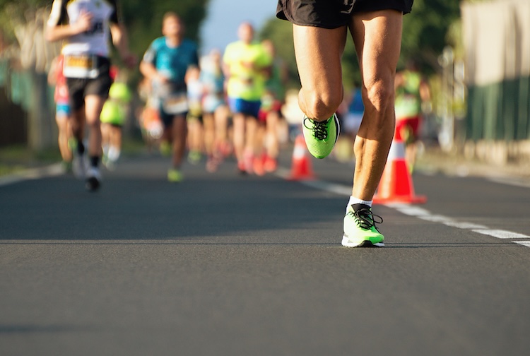Low view of runners on a street, showing their knees and bright colored shoes.