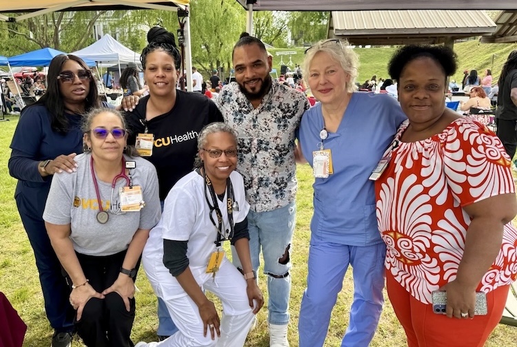 Group of VCU Health team members in medical scrubs and VCU Health shirts under a tent at an event.
