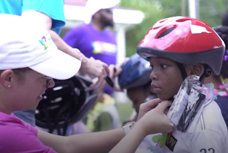 CHoR team member fits a little boy with a red helmet and shows him how to wear it.