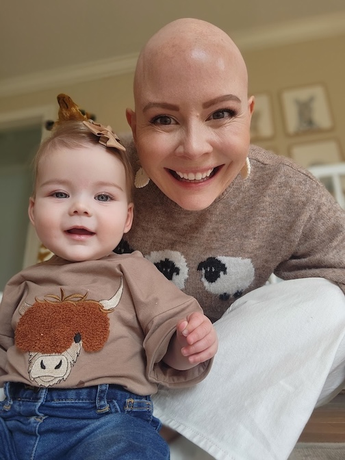 Breast cancer survivor smiles with her baby, both have nearly bald heads