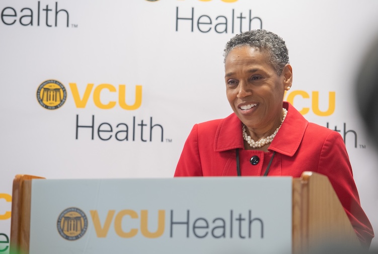 Sheryl Garland stands at a podium in a red suit jacket