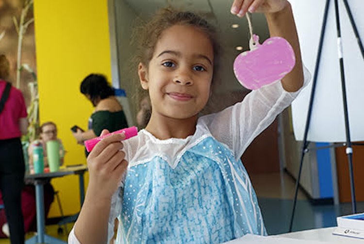 Girl wearing a princess costumes holding up colored paper pumpkin.
