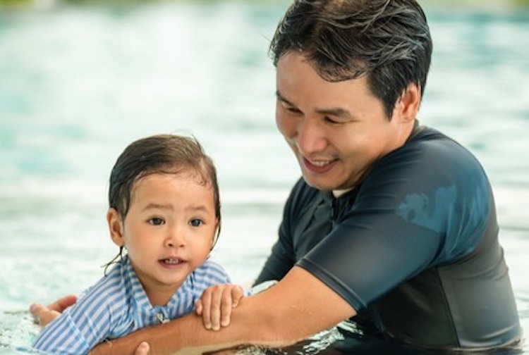 Father holding small child while he teaches her how to swim in a pool (Getty Images)