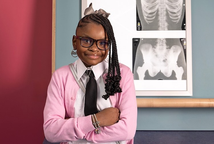 Tamiyah standing with arms folded in front of an x-ray photo wearing a pink sweater.