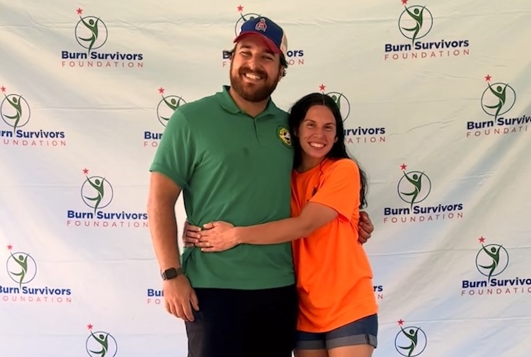Burn survivor and wife, who is a burn nurse, hug in front of a sign for the foundation