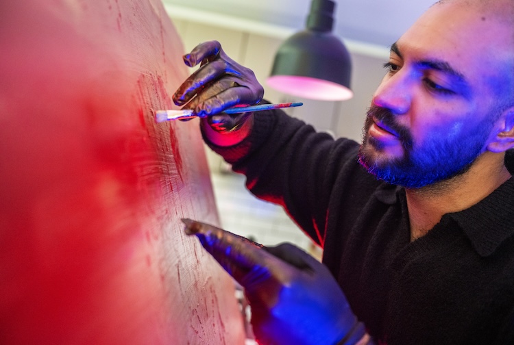 Dr. Khan uses red paint while wearing with gloves, up close to the canvas