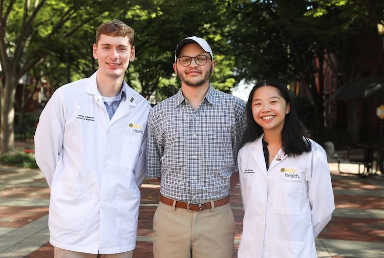 Three VCU students stand together, two of them are in medical white coats signifying that they are in medical school.