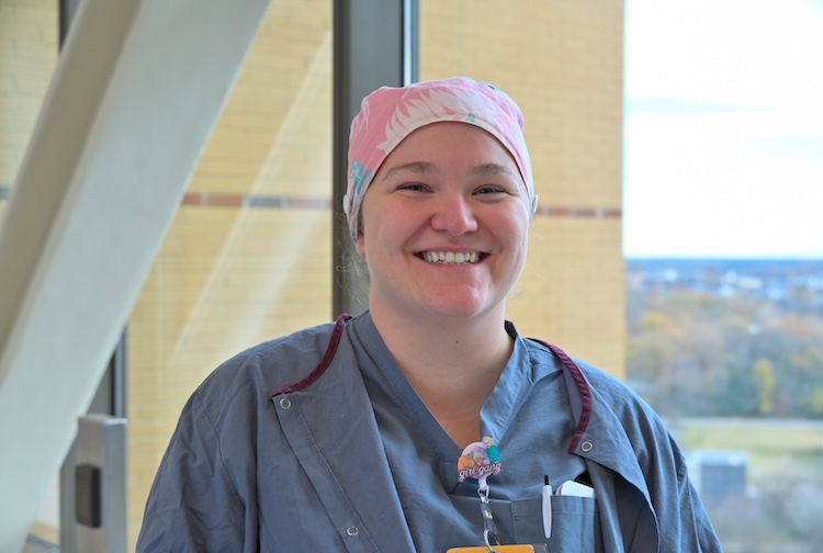 Greer smiles while wearing scrubs and a hair cap