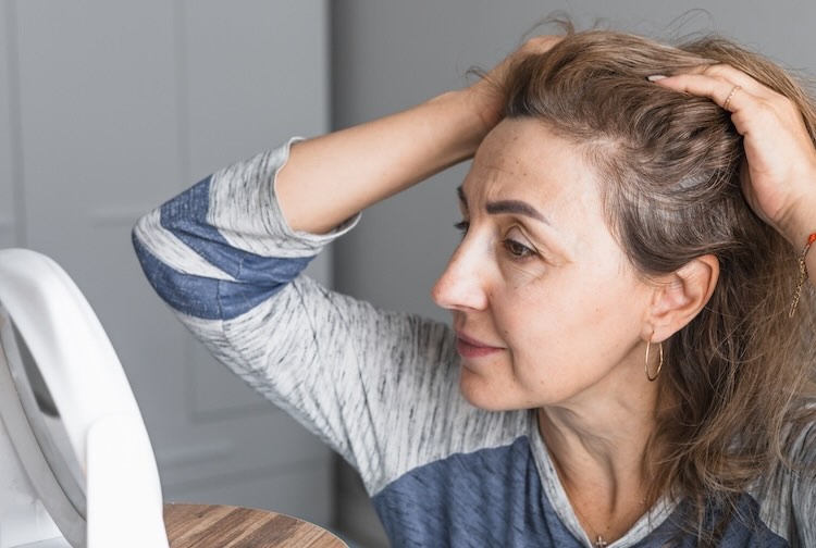 Mature woman inspects her appearance in mirror, looking at changes in her hairline