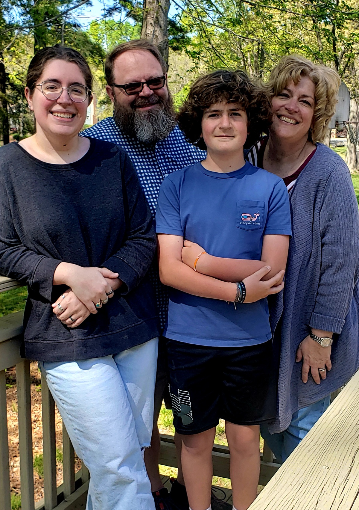 Family of four standing together in a wooded area.
