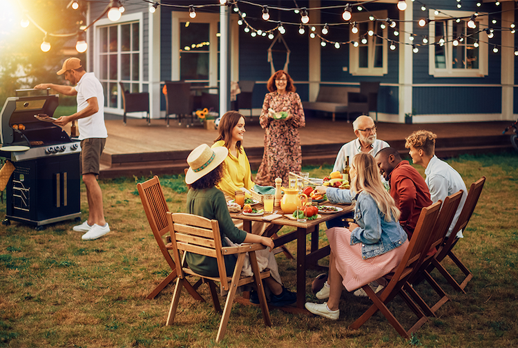 family and friends sit around a table in a backyard while grilling dinner