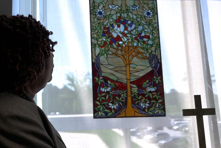Woman looking at a cross with a stained glass in the window