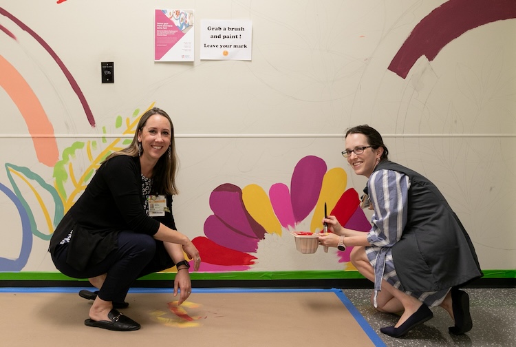 two women kneeling and smiling while painting a caterpillar