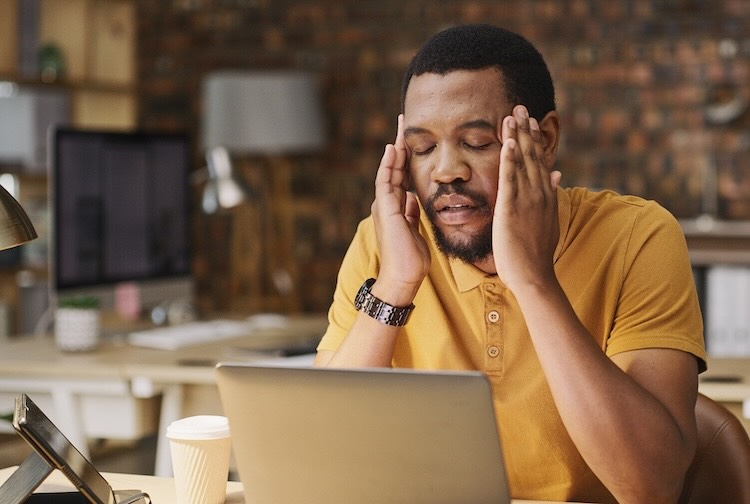 Man working on a laptop is experiencing a headache and holds his head.