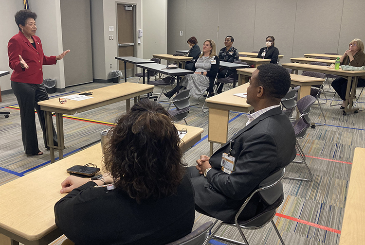 A lady in a red blazer speaks to health care workers in a classroom setting