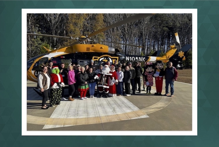 People dressed as Mickey and Minnie Mouse along with the Grinch pose with a group of hospital employees and their families in front of a helicopter.