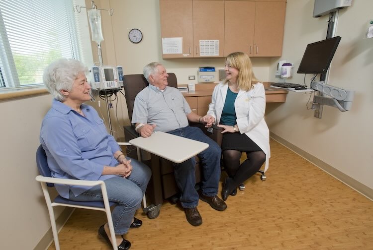 Dr. Hackney holds a patient’s hand while talking about cancer treatment. His partner smiles during their conversation.