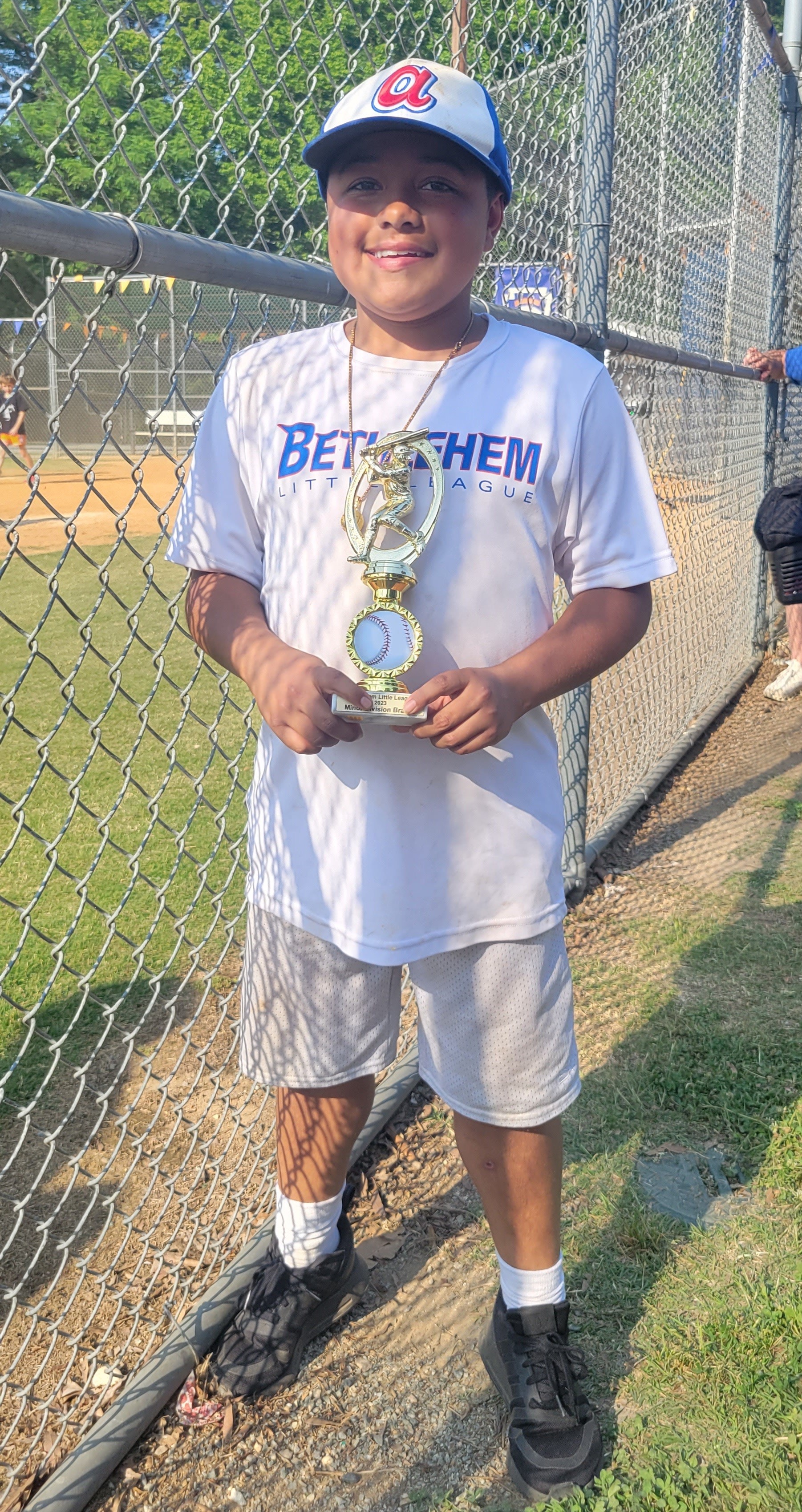 Young boy smiling while wearing a little league baseball uniform.