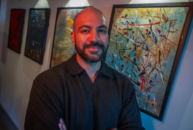 Dr. Khan stands in front of a wall of his abstract art