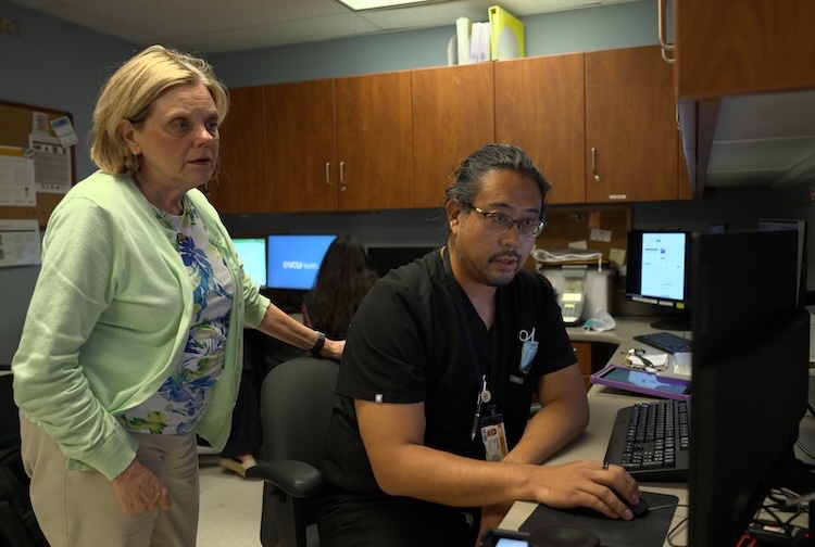 Man sits at a desk with woman looking over shoulder at scans of a patient.