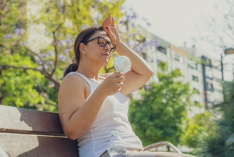 Woman suffering in the heat. Holding an electric mini fan sitting outdoors.
