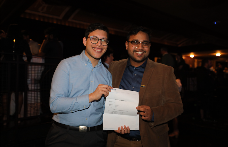 Two men standing with a paper, smiling