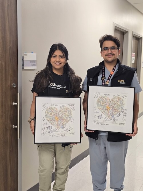 Two family medicine residents at VCU Health Community Memorial Hospital (CMH) display framed heart-shaped maps filled with handwritten messages of encouragement from staff and community members.