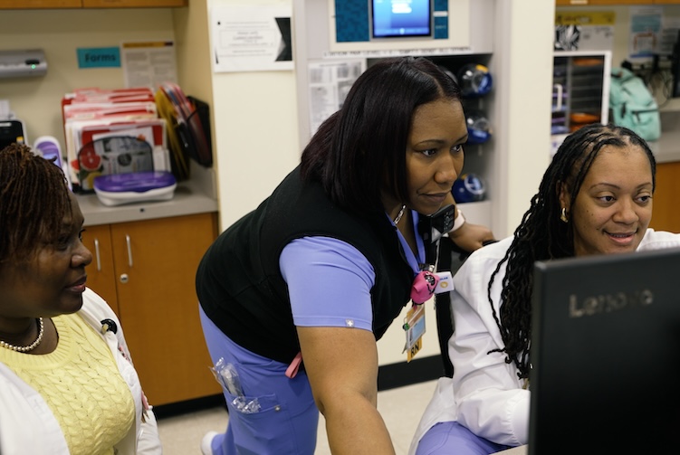 Three VCU Health team members are working in a unit. They are sitting at a desk, filling out patient information together.