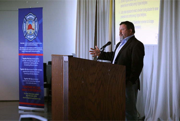 Man in a suit standing at a podium speaking to a crowd.
