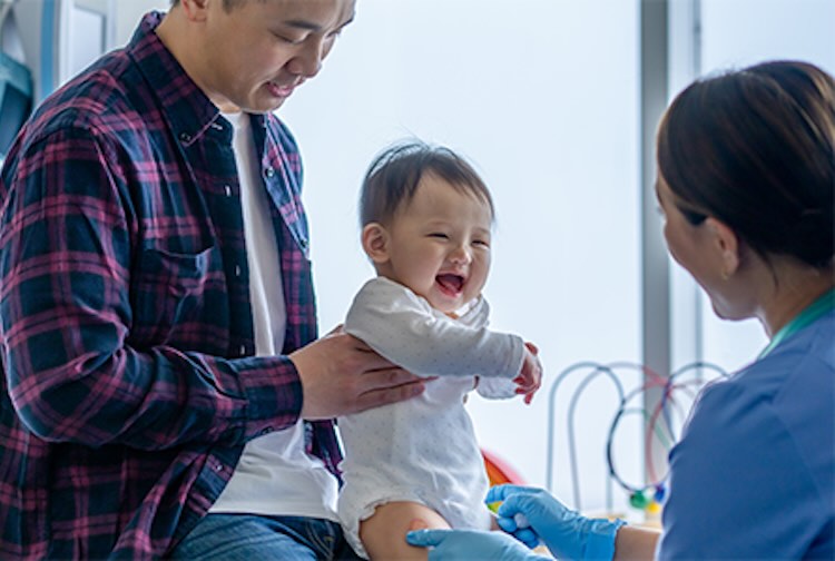 Father holding baby in arms as nurse makes baby smile.