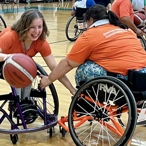women smiling and playing basketball in their wheelchairs