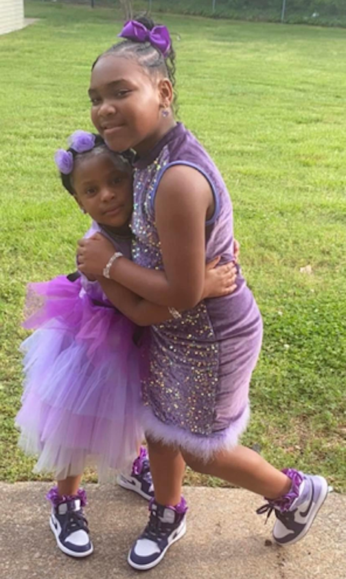 two little girls in purple dresses hug