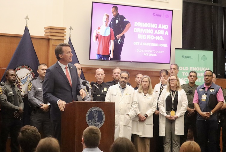 Group stands in front of a crowd, with the governor speaking.