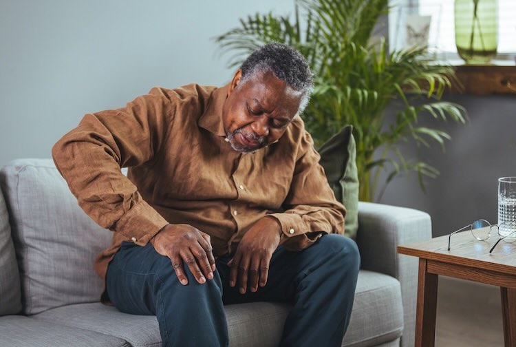 man sitting on a sofa in the living room at home and touching his knee