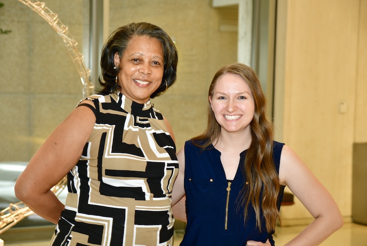 Two women stand next to each other, arm in arm, smiling.