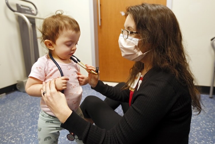 Dr. Kimbrough sits on the floor and lets a toddler wear a stethoscope