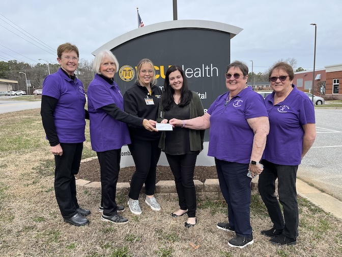  Group of women wearing black or purple shirts stand in front of a hospital sign.
