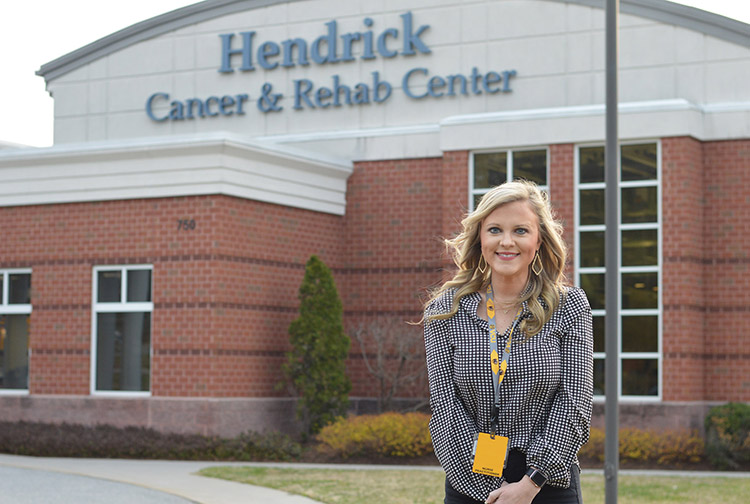 A health care worker stands outside of a brick building.