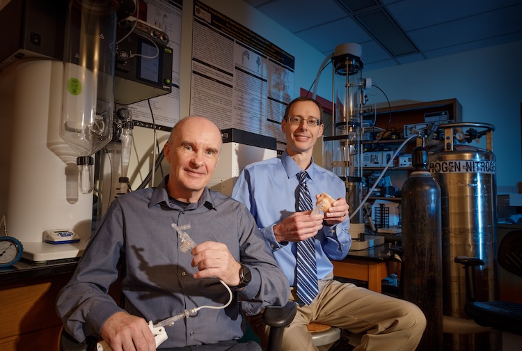 Two male researchers holding equipment in hand in the aerosol research lab.