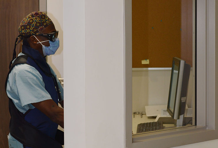 Dr. Mungo wears a lead apron, lead vest, lead glasses and dosimeter while standing behind a lead-plated wall for protection.