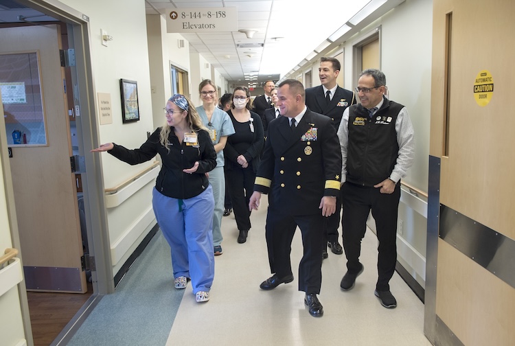 Nurse walking in a hallway leading a tour for about a dozen people.