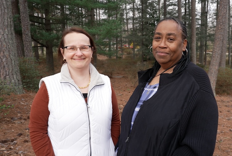 two women smile while wearing fleeces in a park