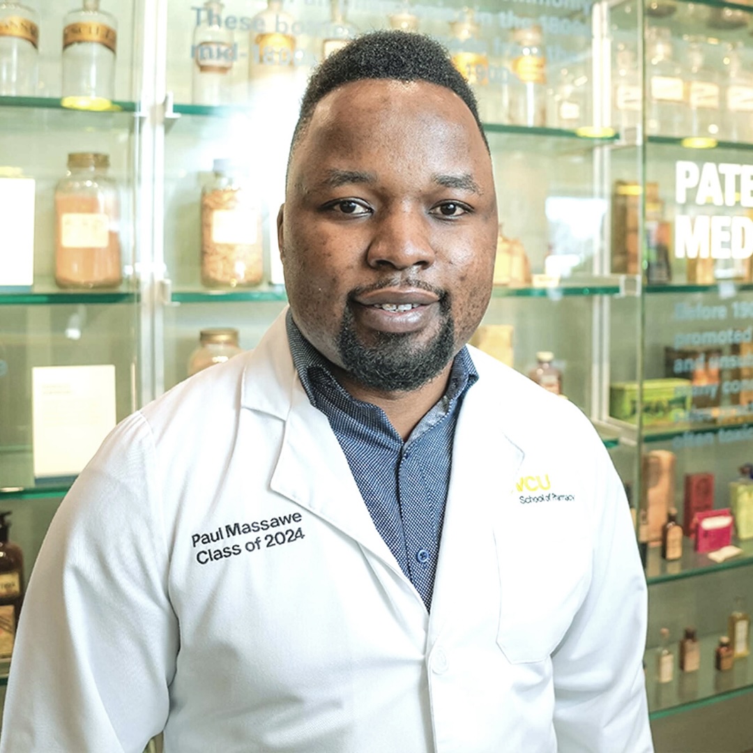 Young man with a pharmacy white coat smiles for the camera. 