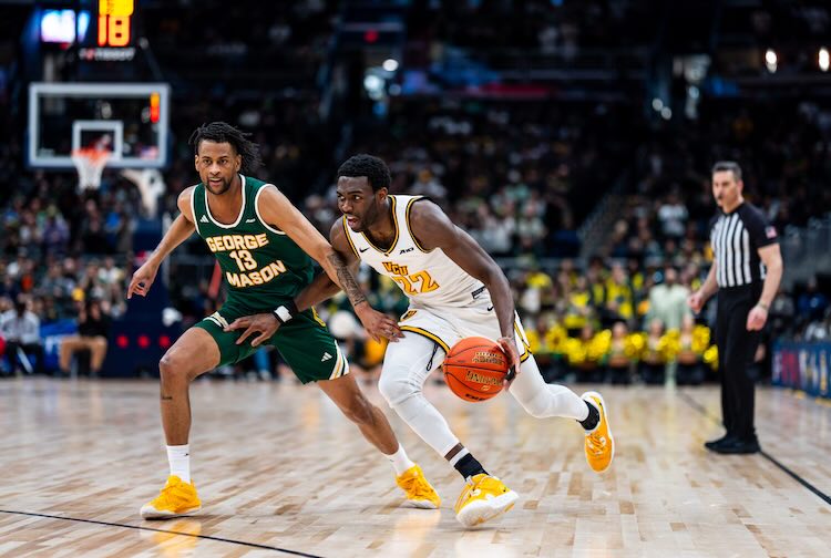Joe Bamisile dribbling up the court while an opposing player tries to block him