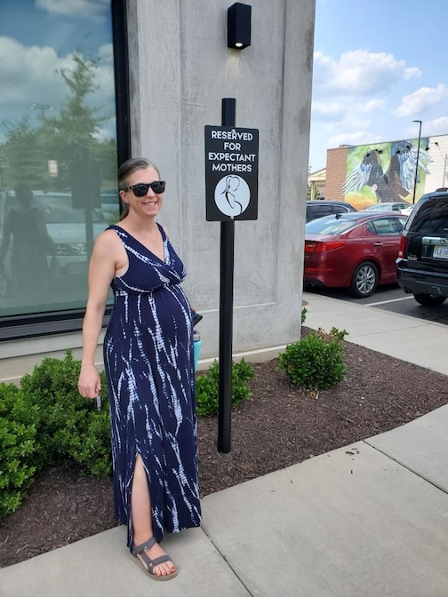 Erin pregnant standing near a parking sign for expecting mothers.