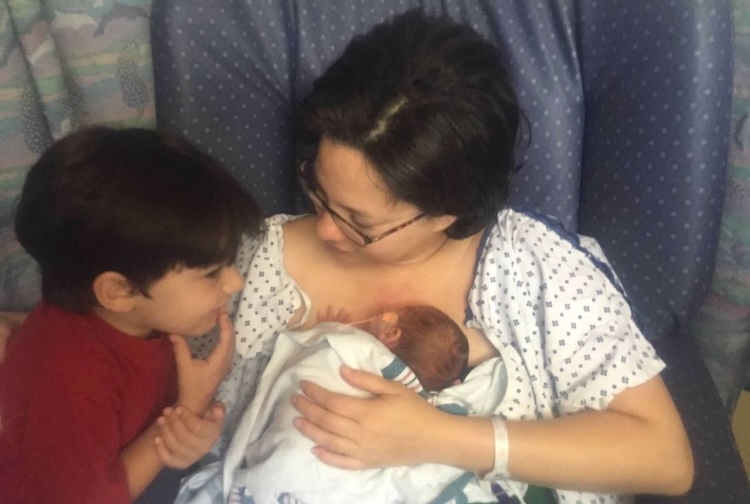 Mother in a hospital bed with a small baby and little boy talking with them